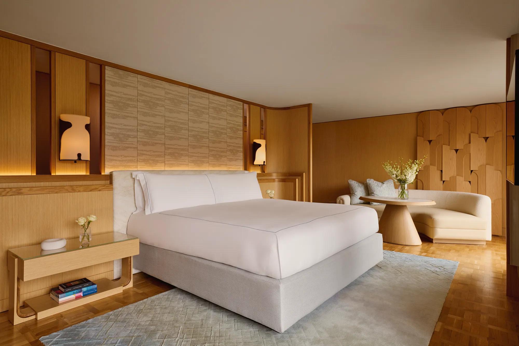 Penthouse bedroom with king bed, wood-panelled walls, curved sofa, and soft lighting