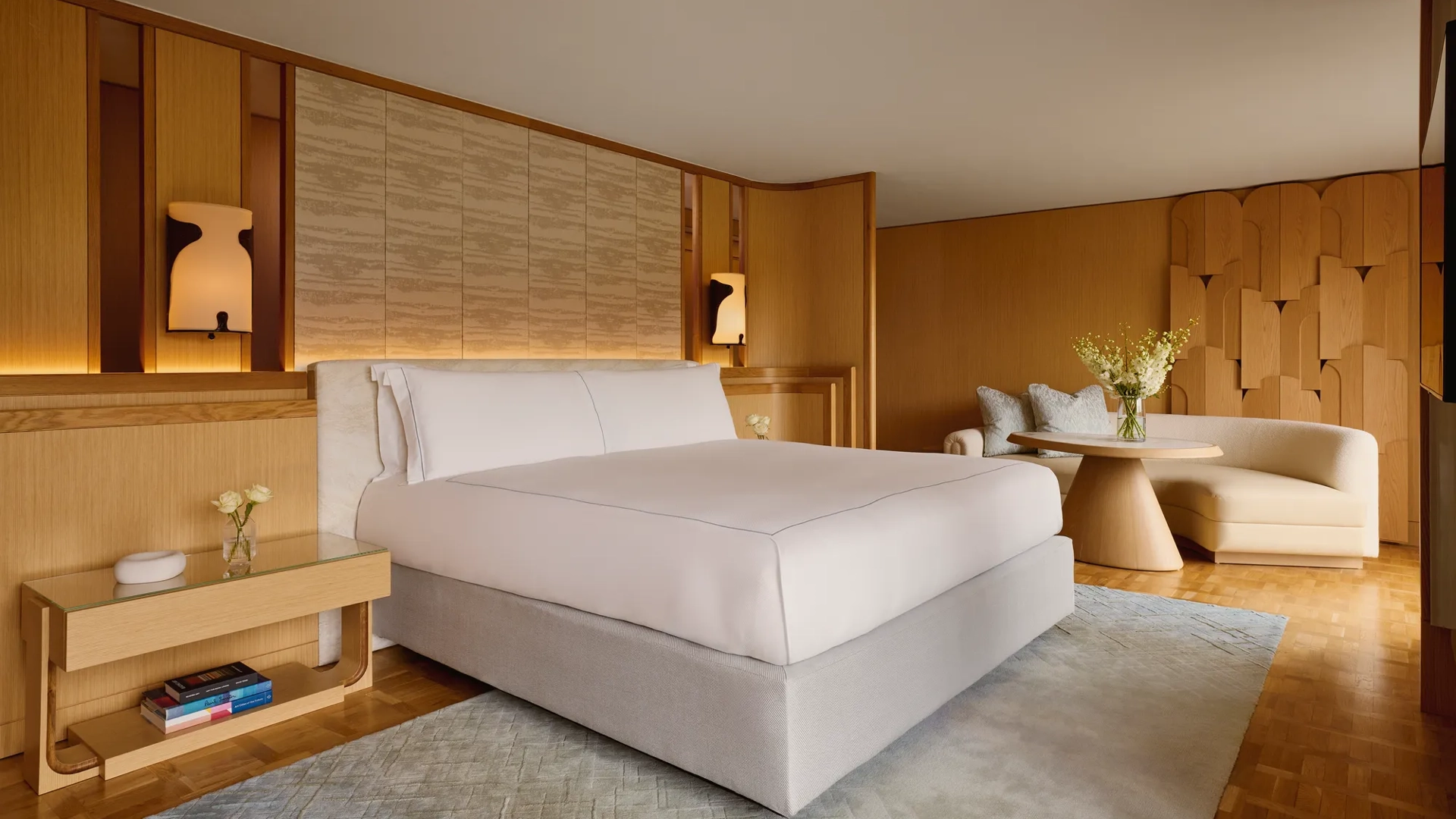 Penthouse bedroom with king bed, wood-panelled walls, curved sofa, and soft lighting