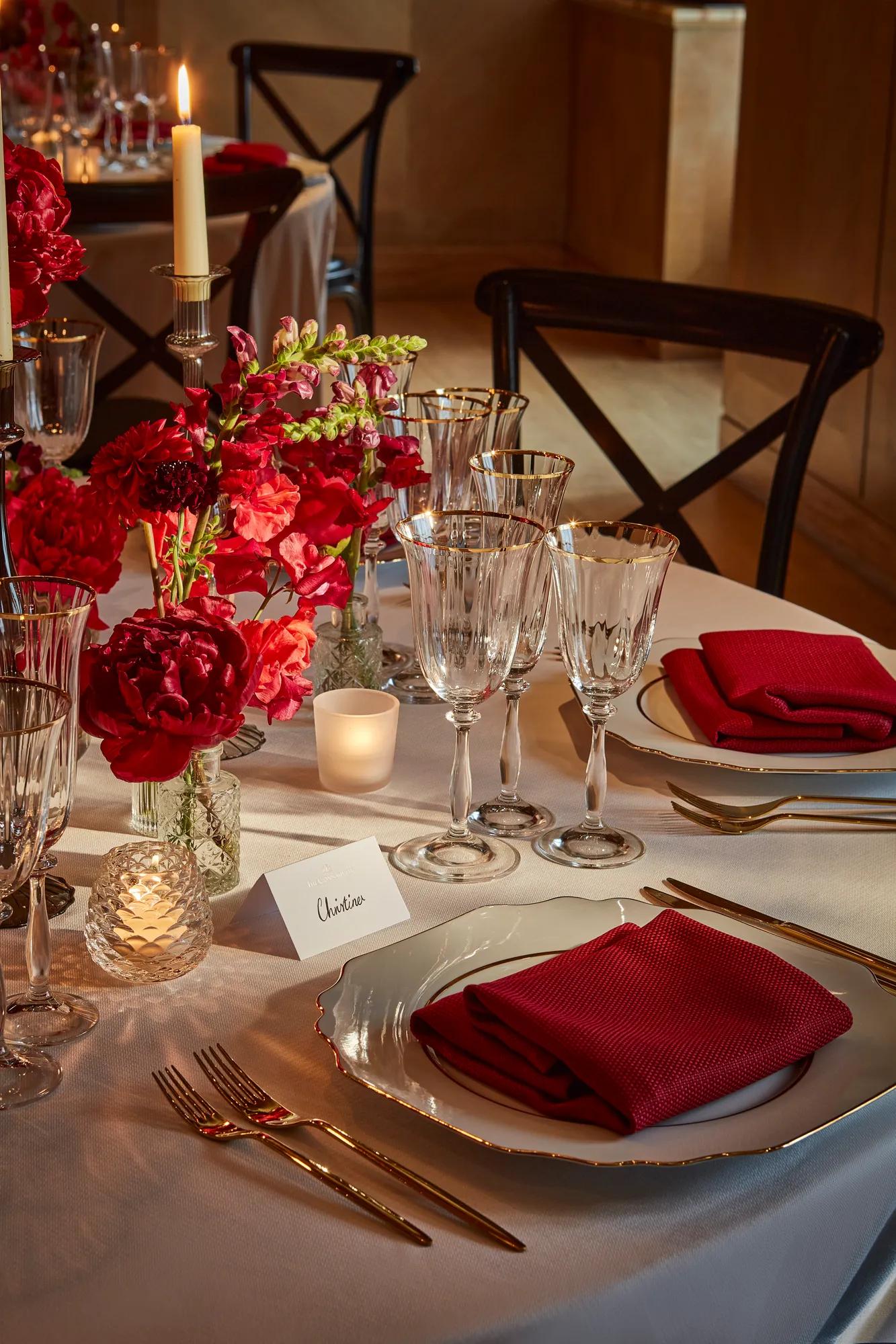 Elegant place setting with red napkin, crystal glassware, and red floral centerpiece.