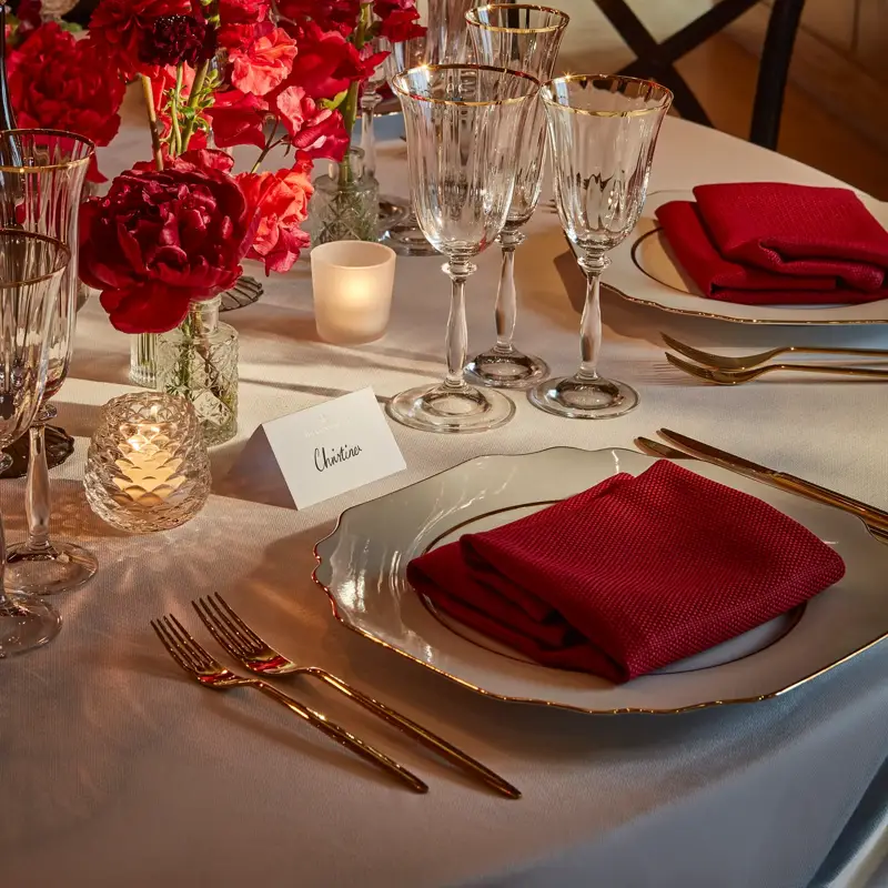 Elegant place setting with red napkin, crystal glassware, and red floral centerpiece.