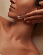 Close-up of therapist applying cream to woman’s jawline during facial treatment, warm lighting highlighting smooth skin and relaxed expression.