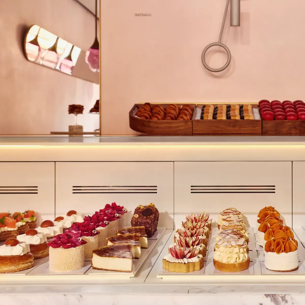 Display case of assorted pastries and tarts in a pastel-pink patisserie, with rows of colorful, finely decorated desserts.
