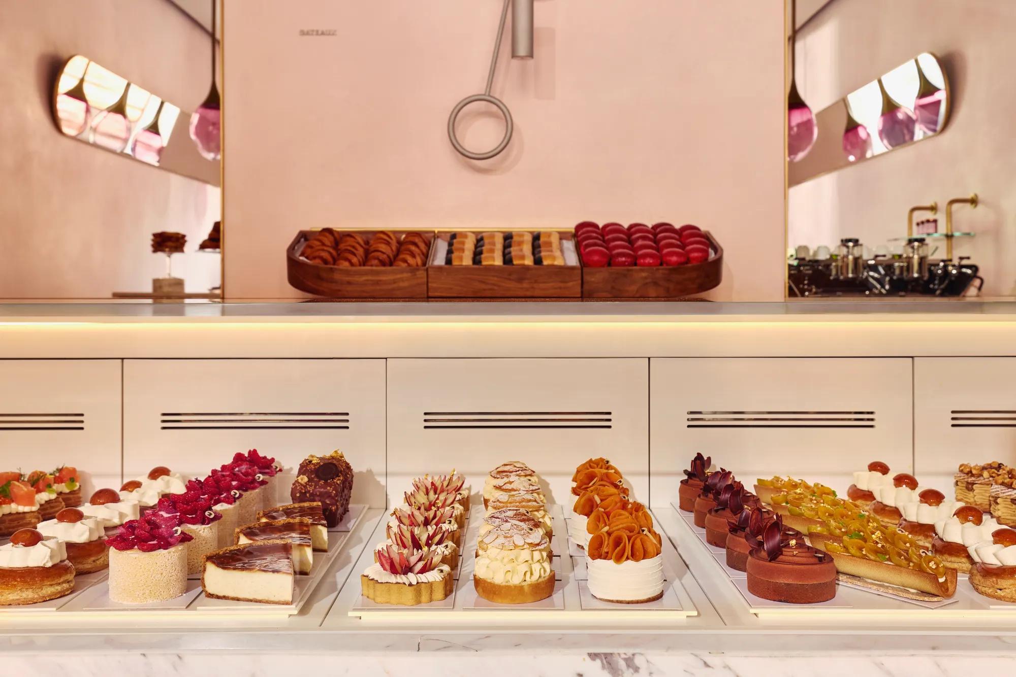 Display case of assorted pastries and tarts in a pastel-pink patisserie, with rows of colorful, finely decorated desserts.