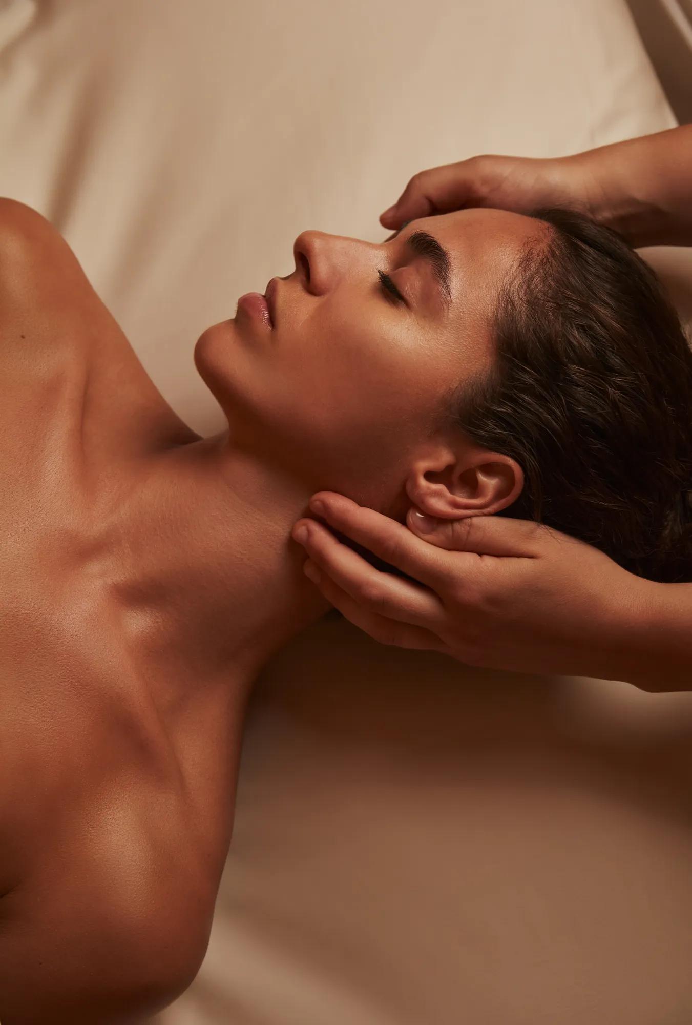 Woman receiving a relaxing spa massage, therapist’s hands supporting her head and neck.