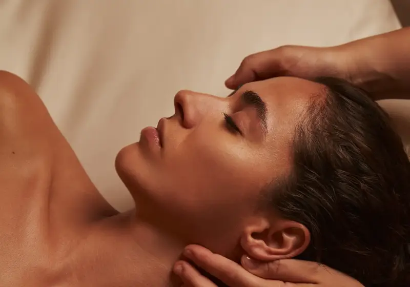 Woman receiving a relaxing spa massage, therapist’s hands supporting her head and neck.