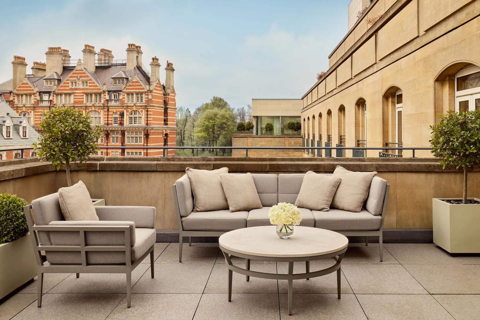 Spacious terrace with beige outdoor seating, round table, and city views including historic red-brick building and greenery
