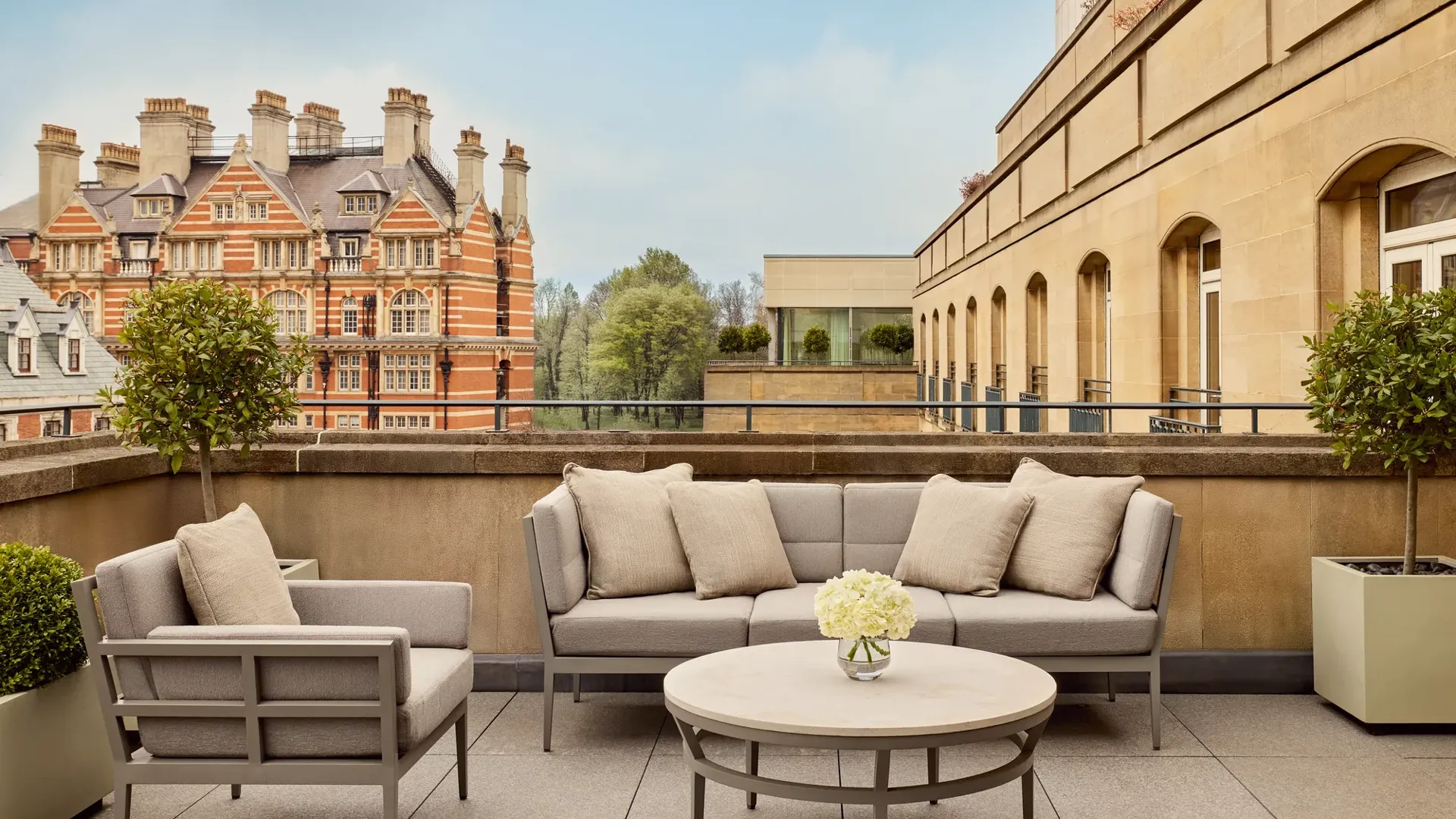 Spacious terrace with beige outdoor seating, round table, and city views including historic red-brick building and greenery