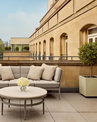 Spacious terrace with beige outdoor seating, round table, and city views including historic red-brick building and greenery