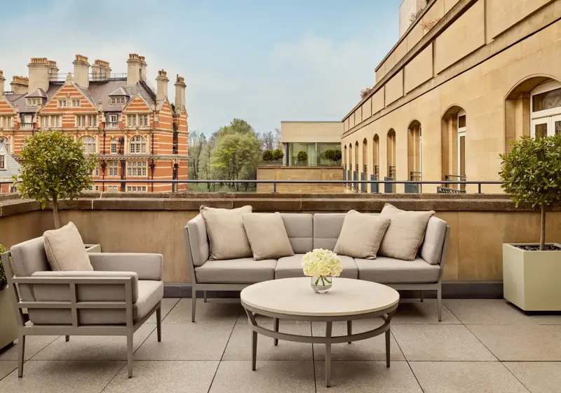Spacious terrace with beige outdoor seating, round table, and city views including historic red-brick building and greenery