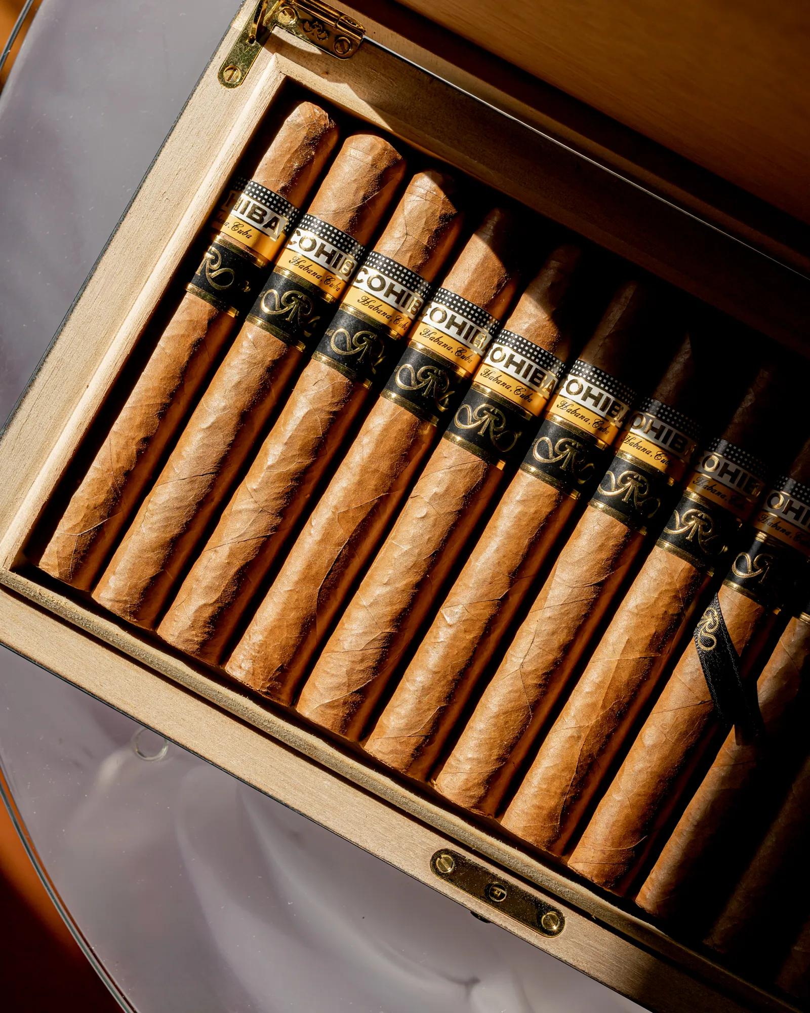 Open wooden box displaying neatly arranged cigars with branded bands in warm light