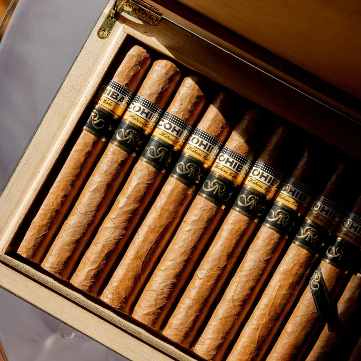 Open wooden box displaying neatly arranged cigars with branded bands in warm light