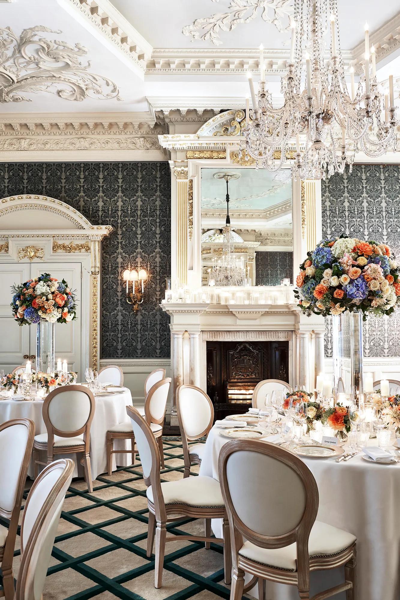 Elegant dining room with crystal chandeliers, floral centrepieces and round tables set for a formal event.