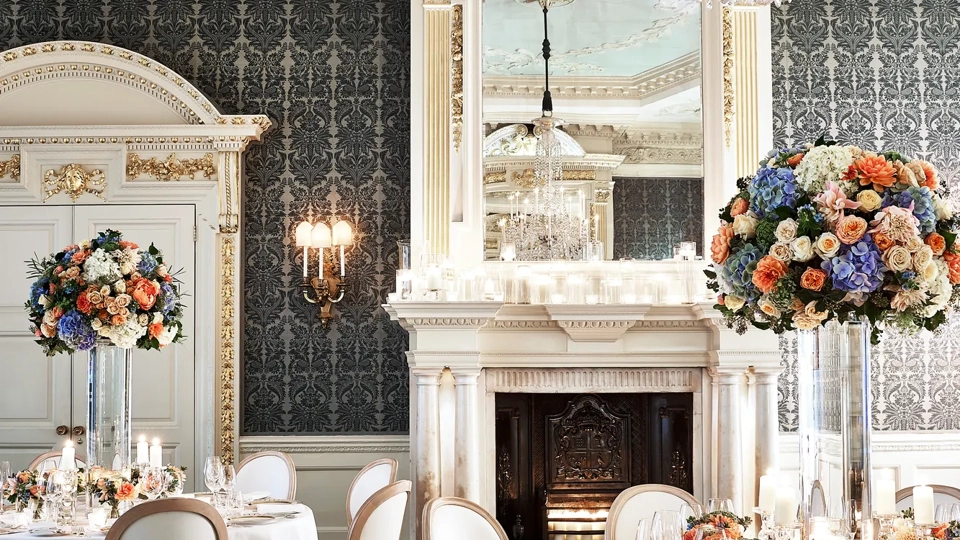 Elegant dining room with crystal chandeliers, floral centrepieces and round tables set for a formal event.