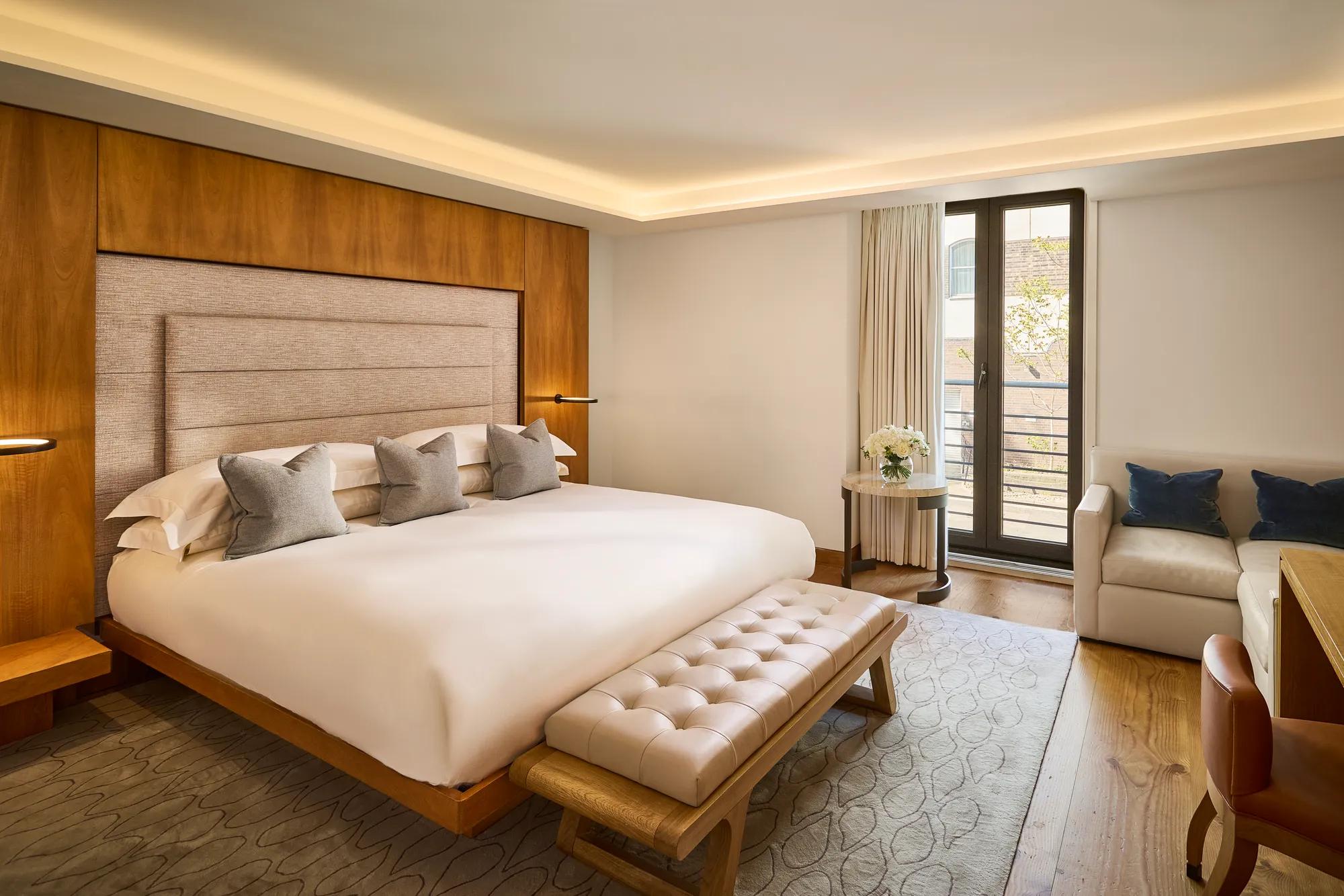 **Alt text:**
Contemporary bedroom with a king-size bed, upholstered bench, seating area, walnut floors and French doors opening to a private balcony.
