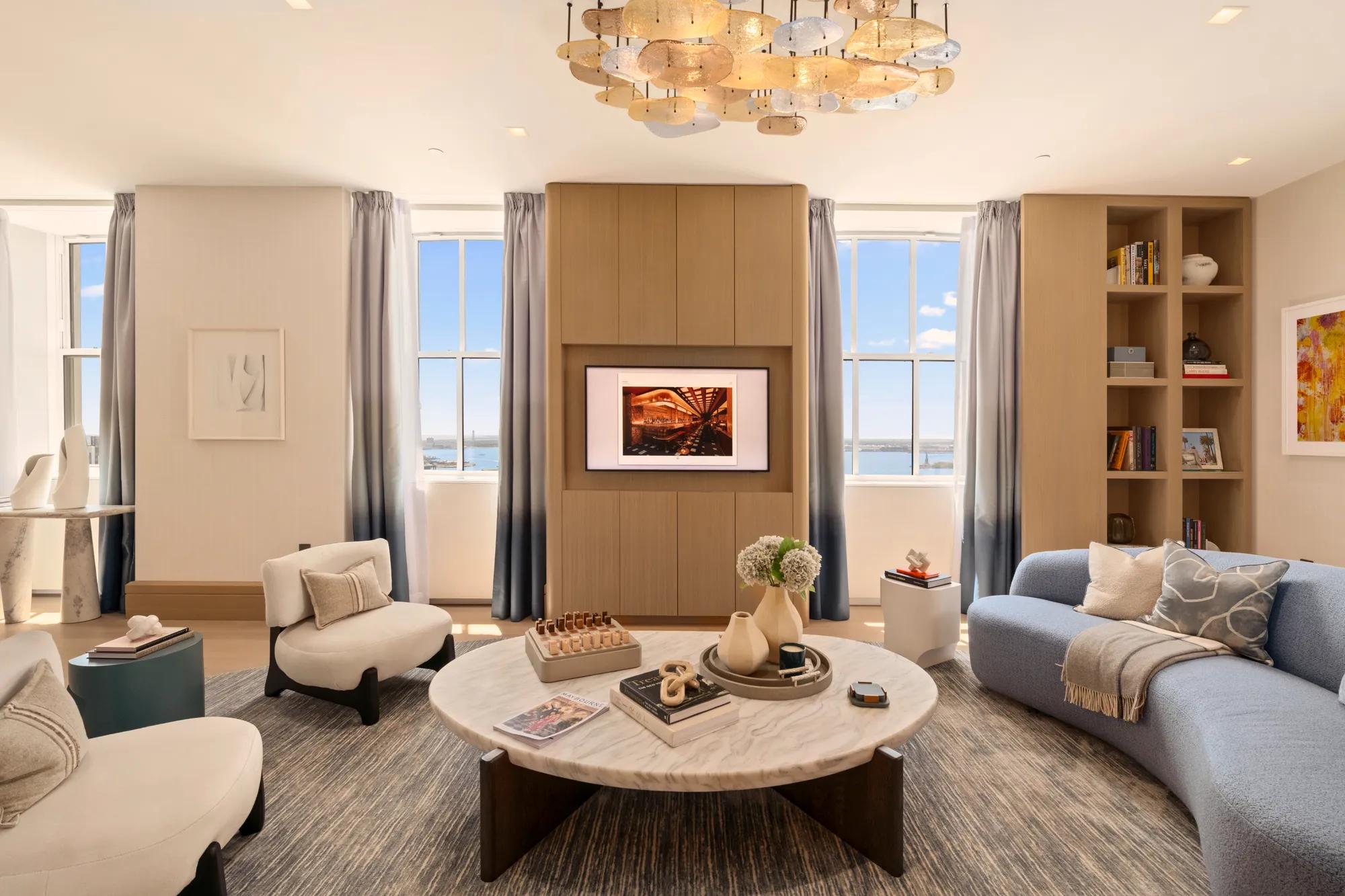 Elegant residential-style living room with curved seating, bespoke cabinetry, marble table and expansive windows overlooking the waterfront.