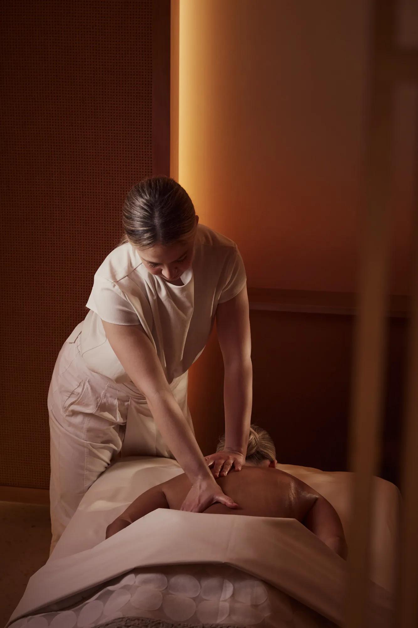 Spa therapist giving a back massage to a guest lying face down on a treatment bed in a softly lit room.