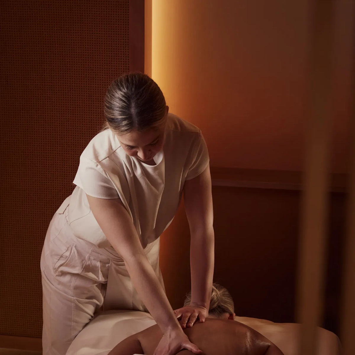 Spa therapist giving a back massage to a guest lying face down on a treatment bed in a softly lit room.