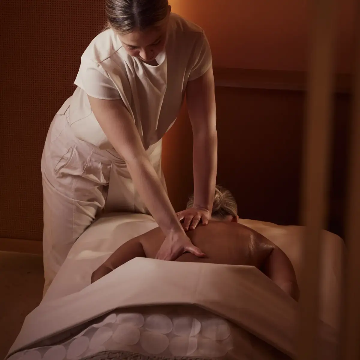 Spa therapist giving a back massage to a guest lying face down on a treatment bed in a softly lit room.