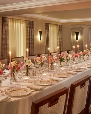 Elegant private dining setup at Claridge’s with a long candlelit table surrounded by upholstered chairs, decorated with pink and white floral arrangements and fine china on crisp white linen.