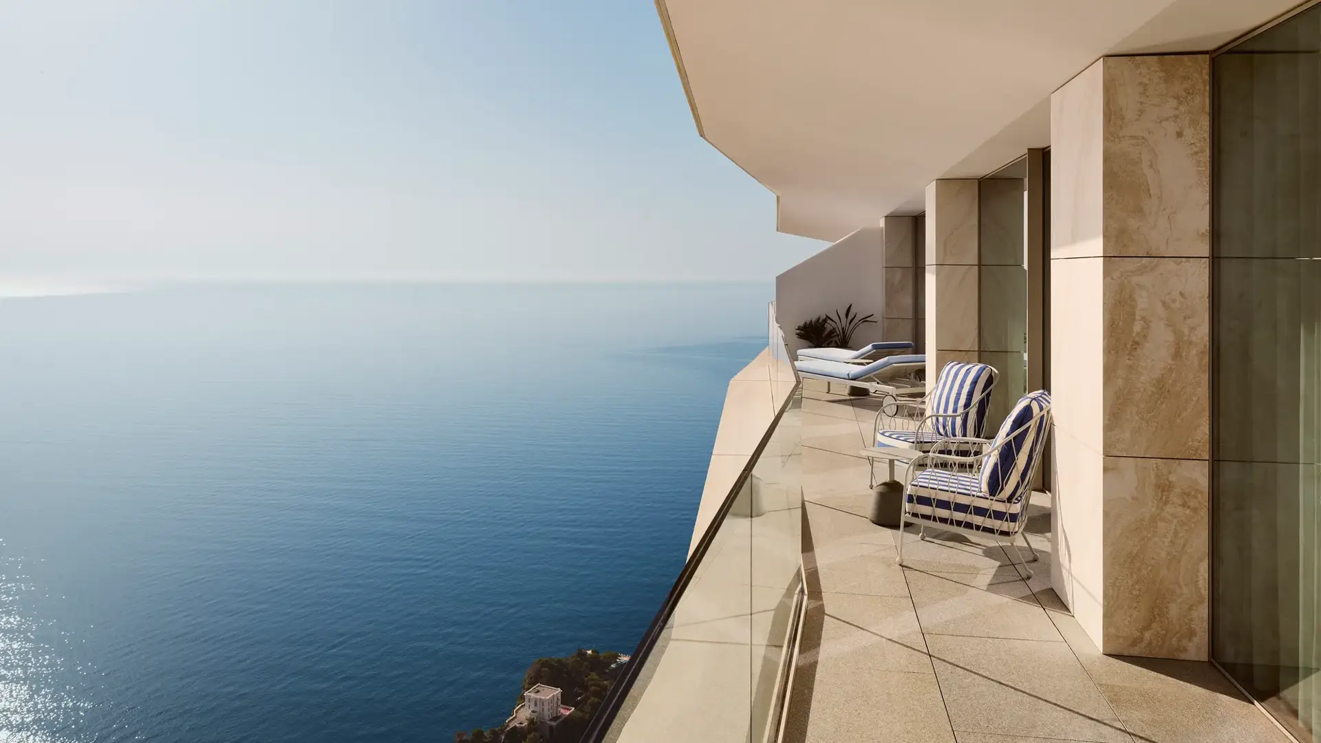 Private balcony with striped lounge chairs overlooking the sea from a modern coastal building.