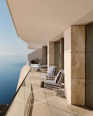 Private balcony with striped lounge chairs overlooking the sea from a modern coastal building.