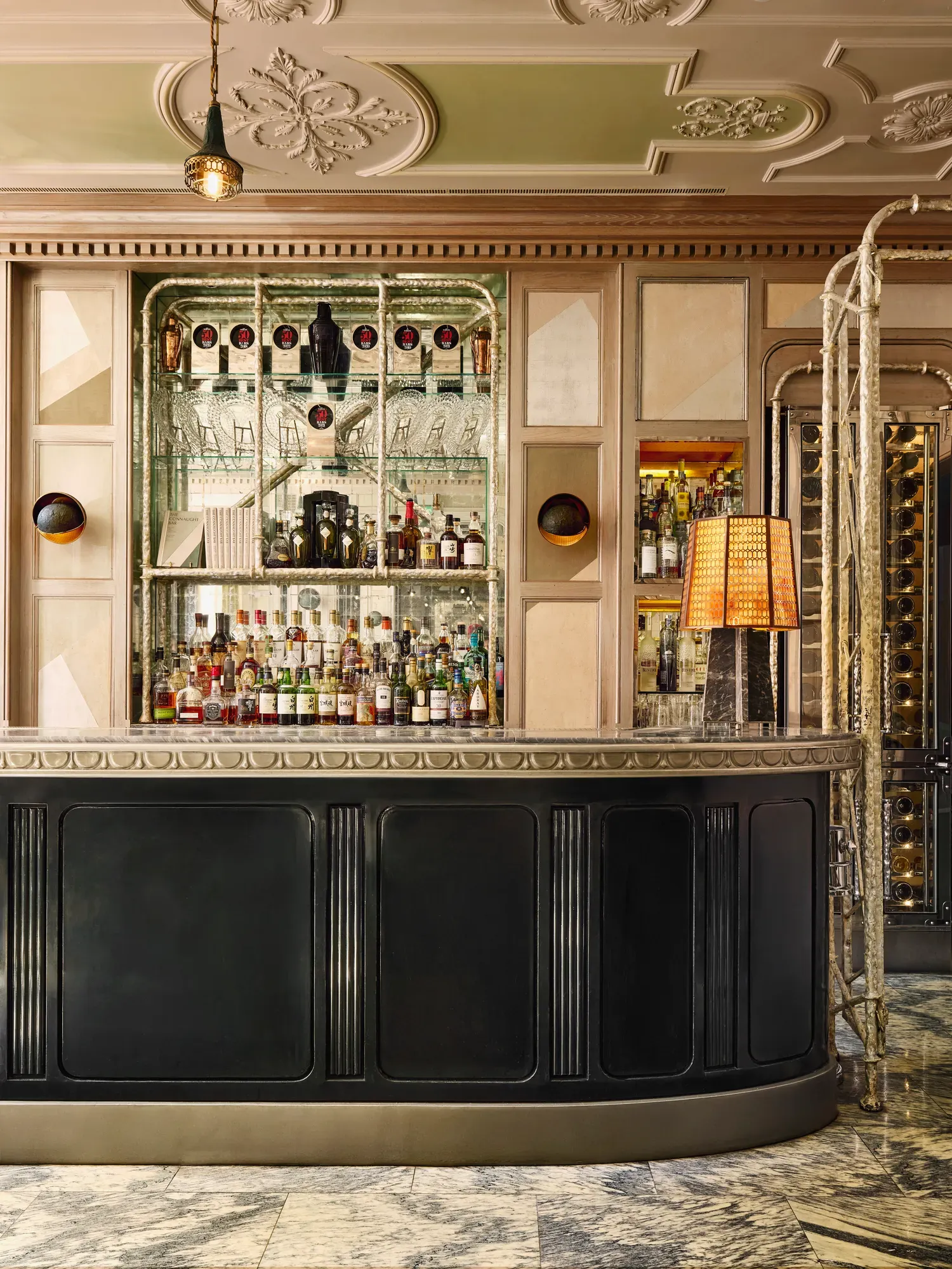 A mirrored back bar with shelves of spirits and glassware, framed by warm panelled walls and a black curved bar counter.
