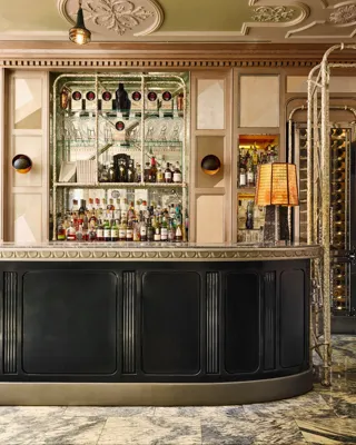 A mirrored back bar with shelves of spirits and glassware, framed by warm panelled walls and a black curved bar counter.