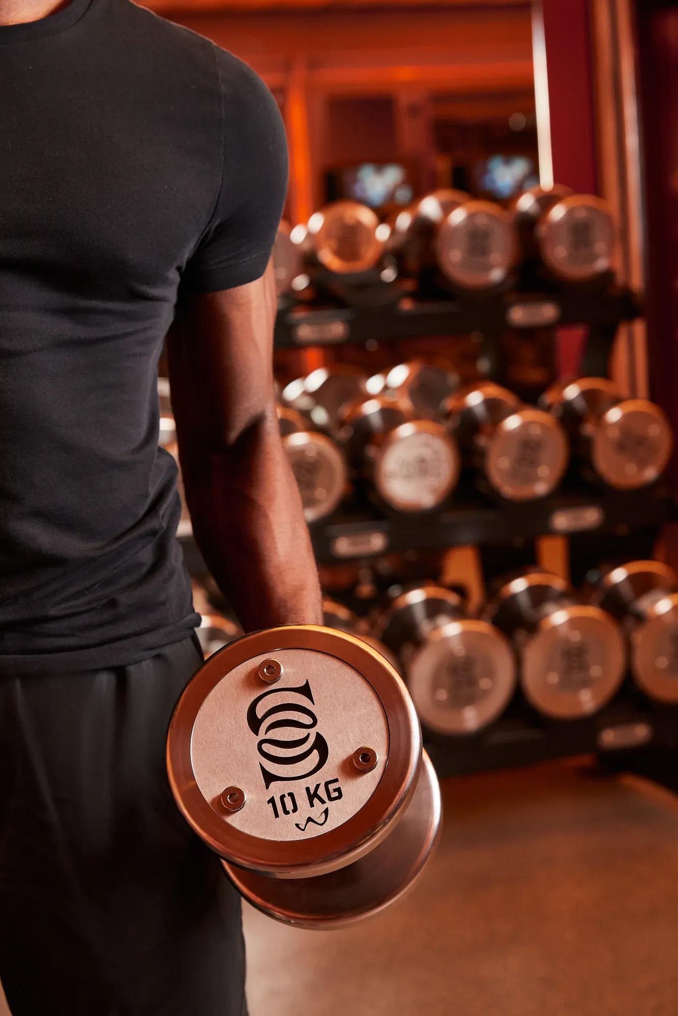 Close-up of a person holding a dumbbell with a 10 kg weight, displaying the Surrenne logo on the side of the dumbbell, with other dumbbells in the background.