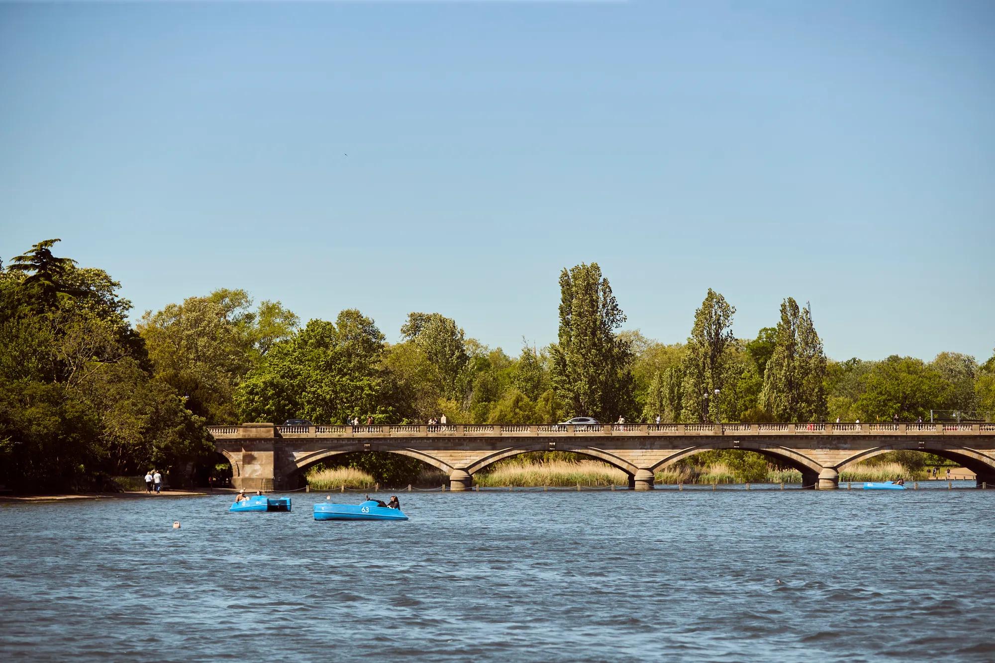 Stone bridge spanning a lake, with pedal boats on the water and trees along the shoreline.