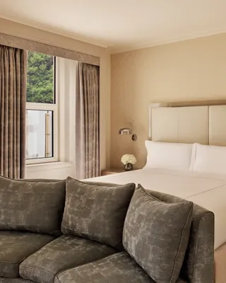 Neutral bedroom with king bed, green sofa, and window view framed by beige curtains.