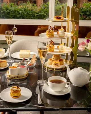 Afternoon tea spread with sandwiches, scones, pastries, tea, and champagne on a marble table beside tulips.