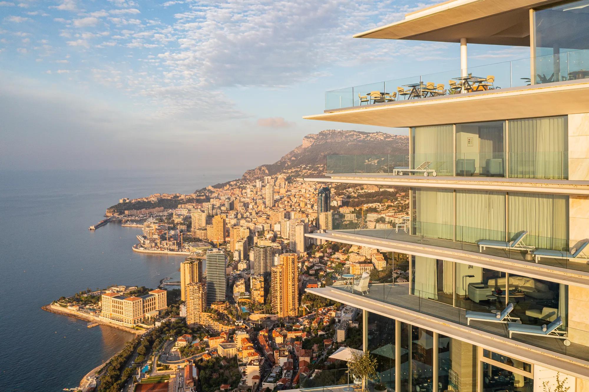 Modern glass terraces overlooking a coastal city skyline and sea at sunrise.