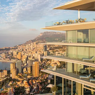 Modern glass terraces overlooking a coastal city skyline and sea at sunrise.