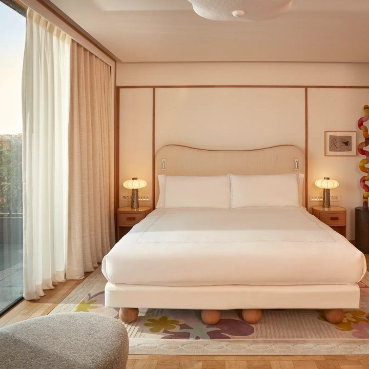 Bright bedroom with a king-size bed, wooden accents, and floor-to-ceiling windows opening onto a private terrace with outdoor seating.