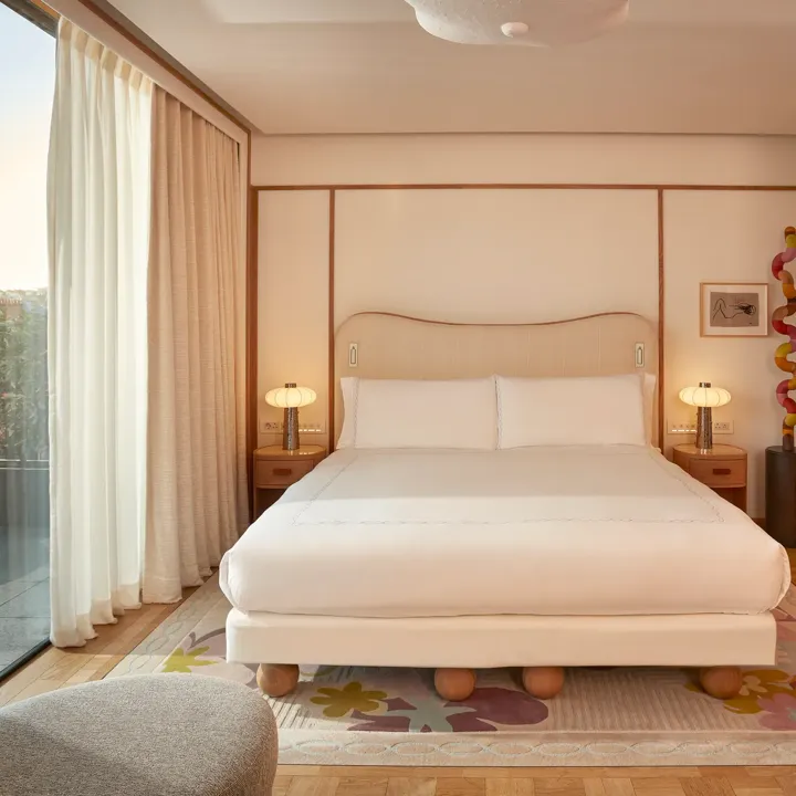 Bright bedroom with a king-size bed, wooden accents, and floor-to-ceiling windows opening onto a private terrace with outdoor seating.