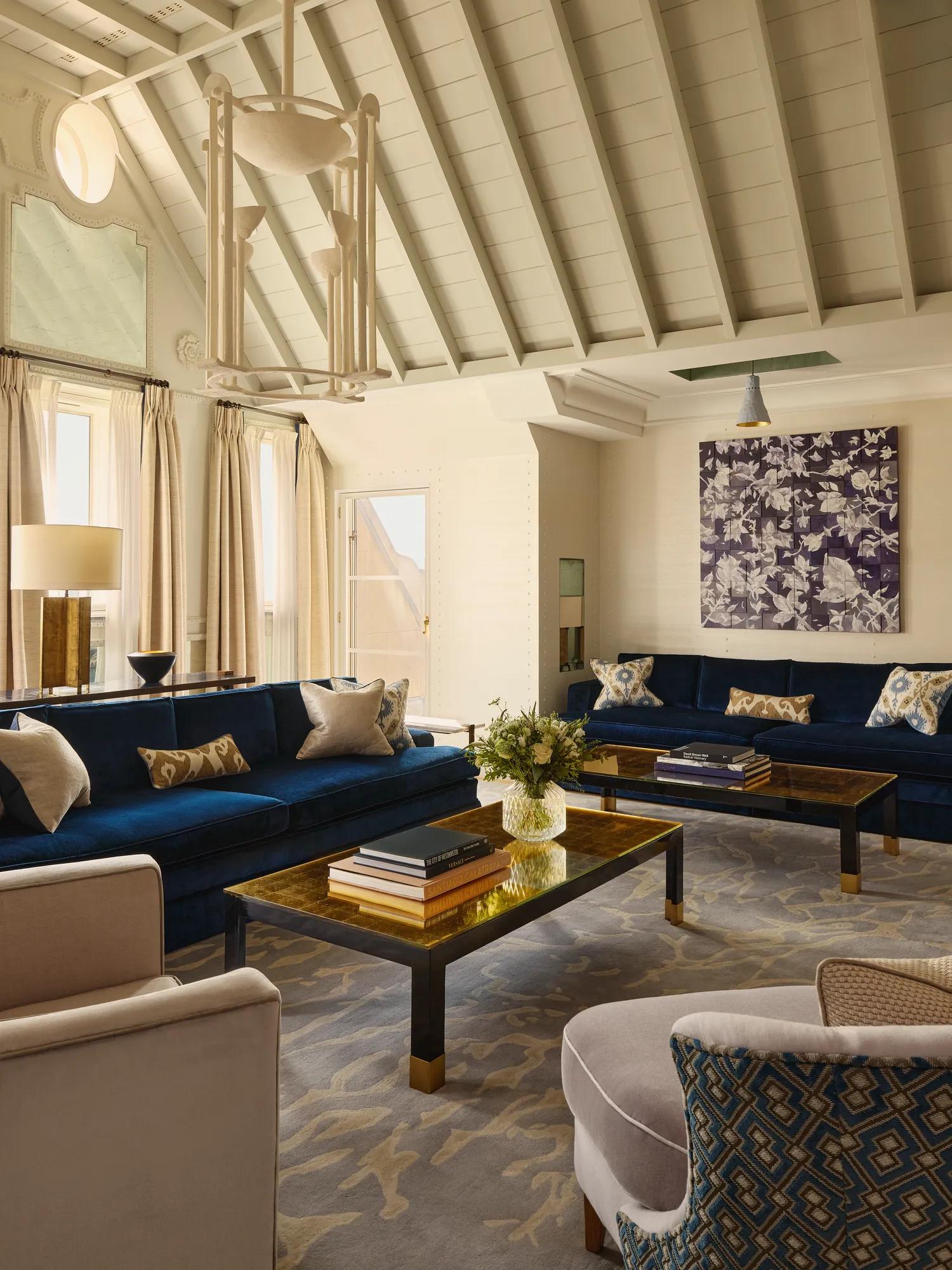 Lofty living room with deep blue sofas, patterned rug, gold coffee tables, and vaulted ceiling.