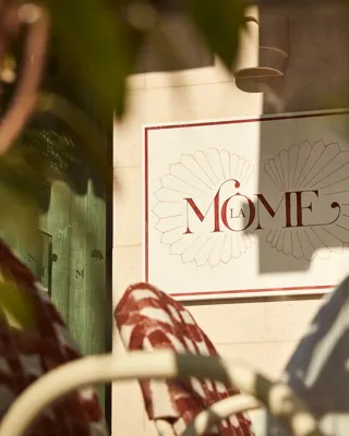 Close-up of La Môme restaurant sign framed by blurred foliage in foreground.