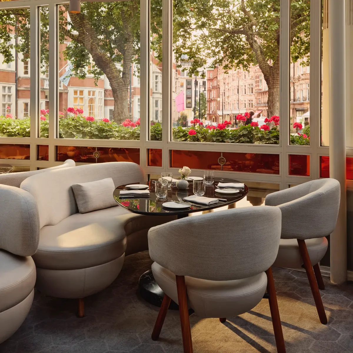 Bright dining alcove with curved white seating, round table, and large windows overlooking trees and flower boxes.