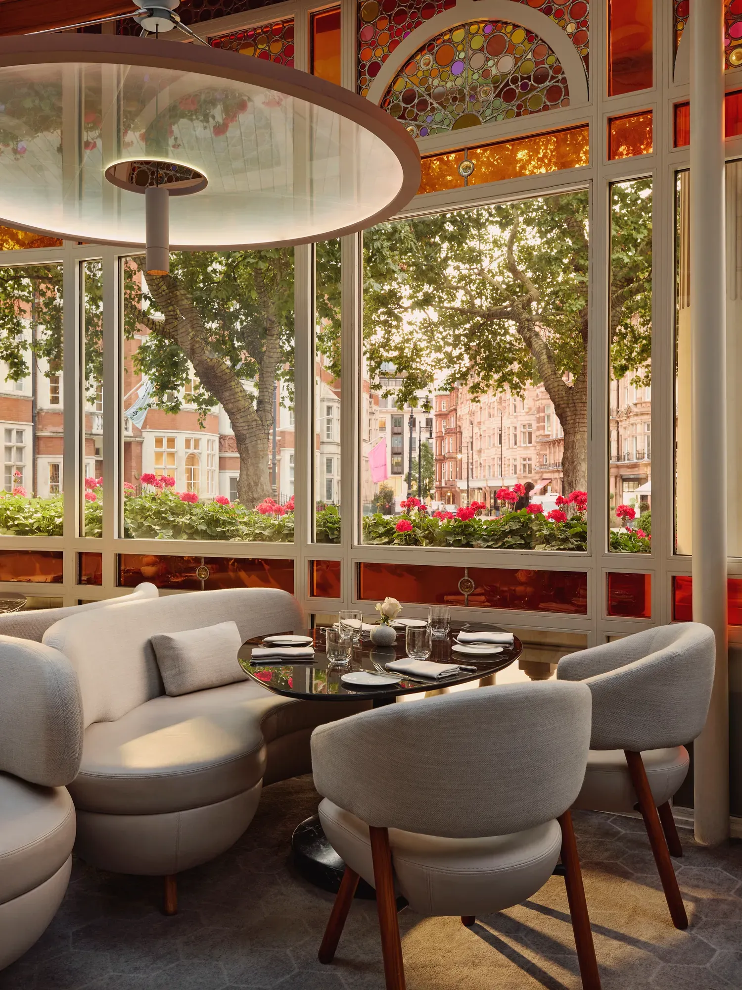 Bright dining alcove with curved white seating, round table, and large windows overlooking trees and flower boxes.