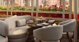 Bright dining alcove with curved white seating, round table, and large windows overlooking trees and flower boxes.