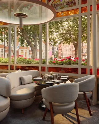 Bright dining alcove with curved white seating, round table, and large windows overlooking trees and flower boxes.