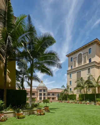 Wide lawn of the Garden Terrace bordered by palms, potted flowers and hotel façades beneath a bright, streaked blue sky.