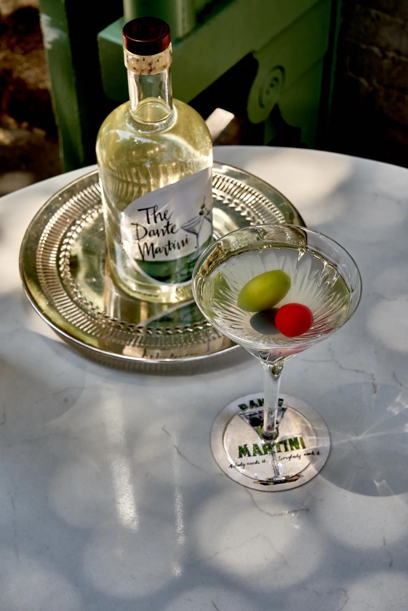 Martini glass with green and red olives beside bottled Dante Martini.