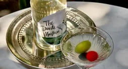Martini glass with green and red olives beside bottled Dante Martini.