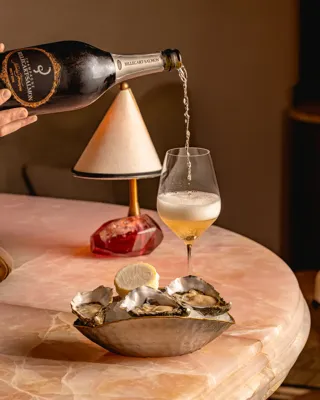 A bottle of champagne tilted over a flute as sparkling wine pours in, creating bubbles that rise to the surface.