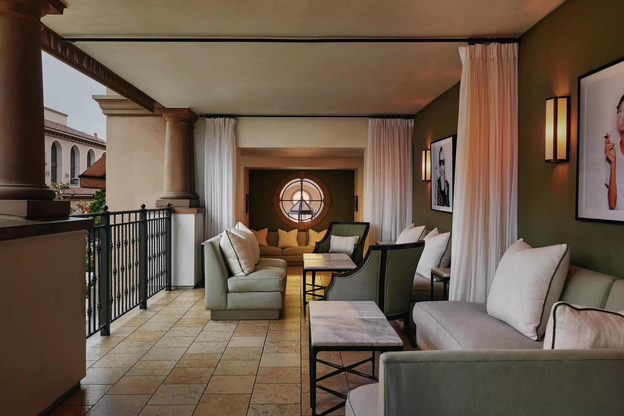 Covered terrace lounge with cushioned sofas, marble tables, and a round window overlooking the courtyard.
