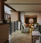 Covered terrace lounge with cushioned sofas, marble tables, and a round window overlooking the courtyard.