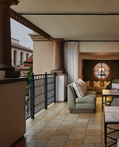 Covered terrace lounge with cushioned sofas, marble tables, and a round window overlooking the courtyard.