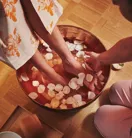 Close-up of a spa therapist washing a guest’s feet in a wooden bowl filled with warm water and rose petals at The Maybourne Riviera.