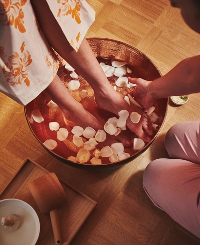 Close-up of a spa therapist washing a guest’s feet in a wooden bowl filled with warm water and rose petals at The Maybourne Riviera.